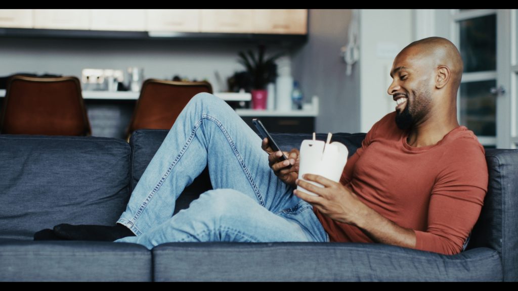 Mann auf dem Sofa mit Smartphone und Kaffeebecher – Look Fuji