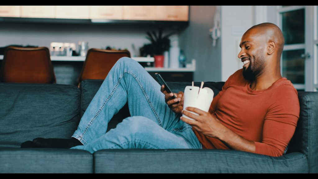 Mann auf dem Sofa mit Smartphone und Kaffeebecher – Look Teal & Orange
