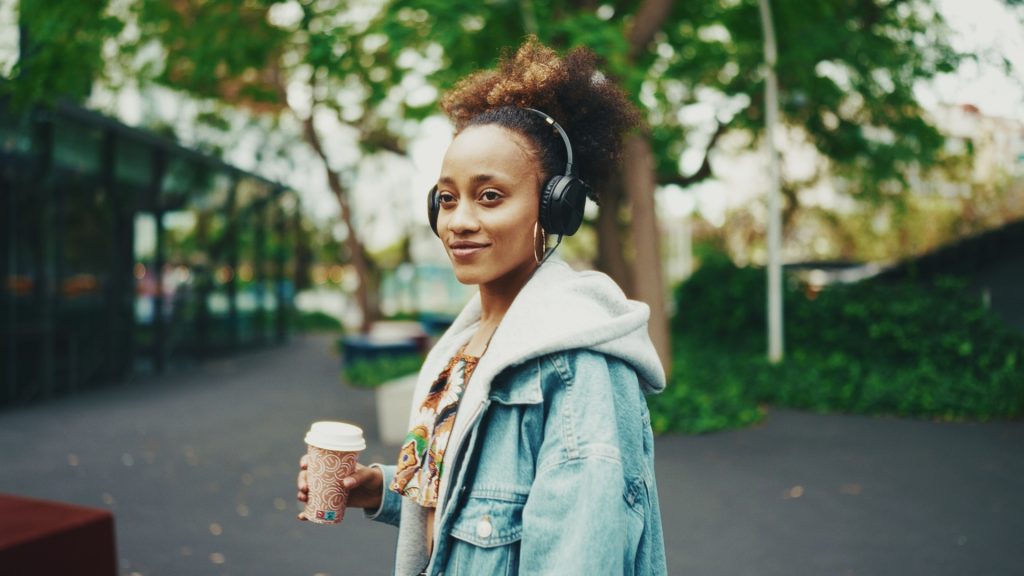 Frau mit Kopfhörern und Kaffeebecher in einer Allee – Look Fuji