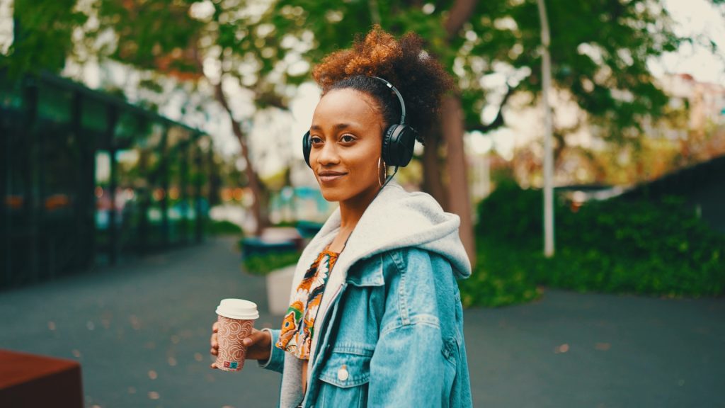 Frau mit Kopfhörern und Kaffeebecher in einer Allee – Look Teal & Orange