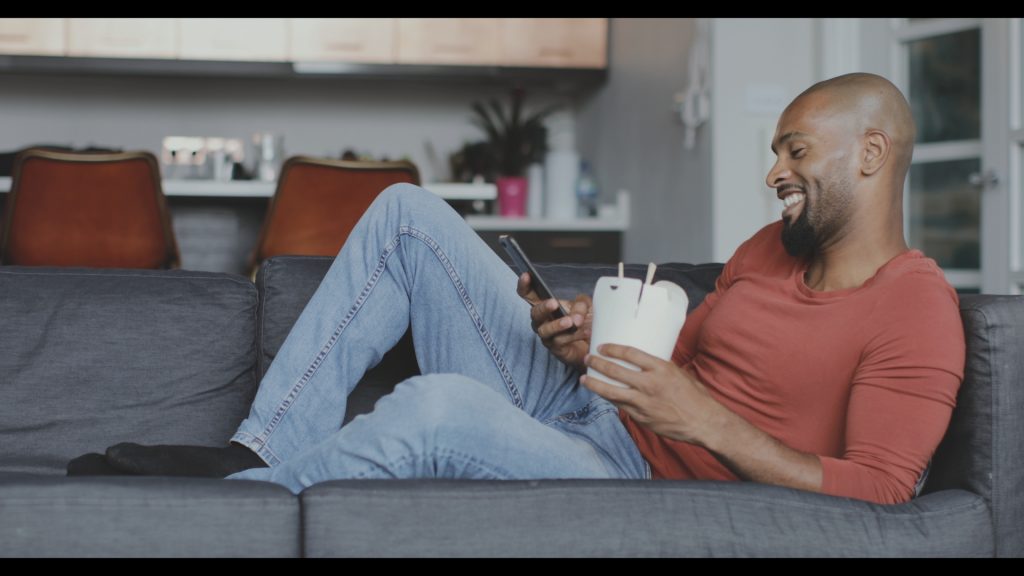 Mann auf dem Sofa mit Smartphone und Kaffeebecher – Original ohne Grading